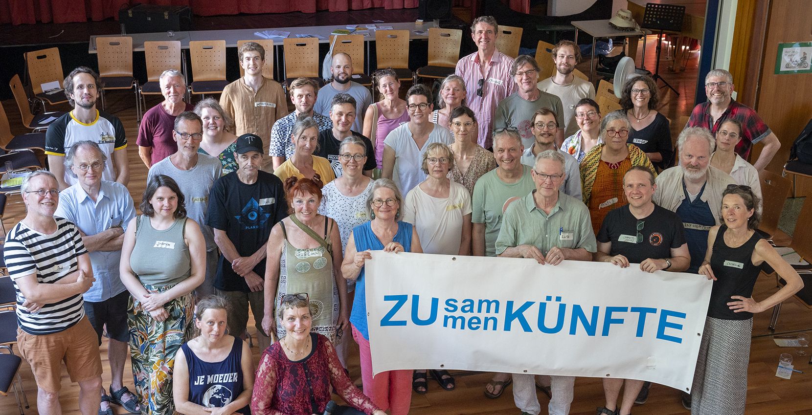 Gruppenbild-Zusammenkunft2 Foto Jo Hempel Bonner Initiativen auf der ZUsammenKUNFt#1 stehen in einer Gruppe und halten ein Banner hoch auf dem steht: ZUsammenKÜNFT